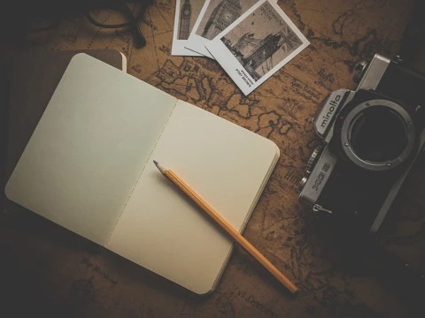 Notebook, pencil, camera and photos on the map