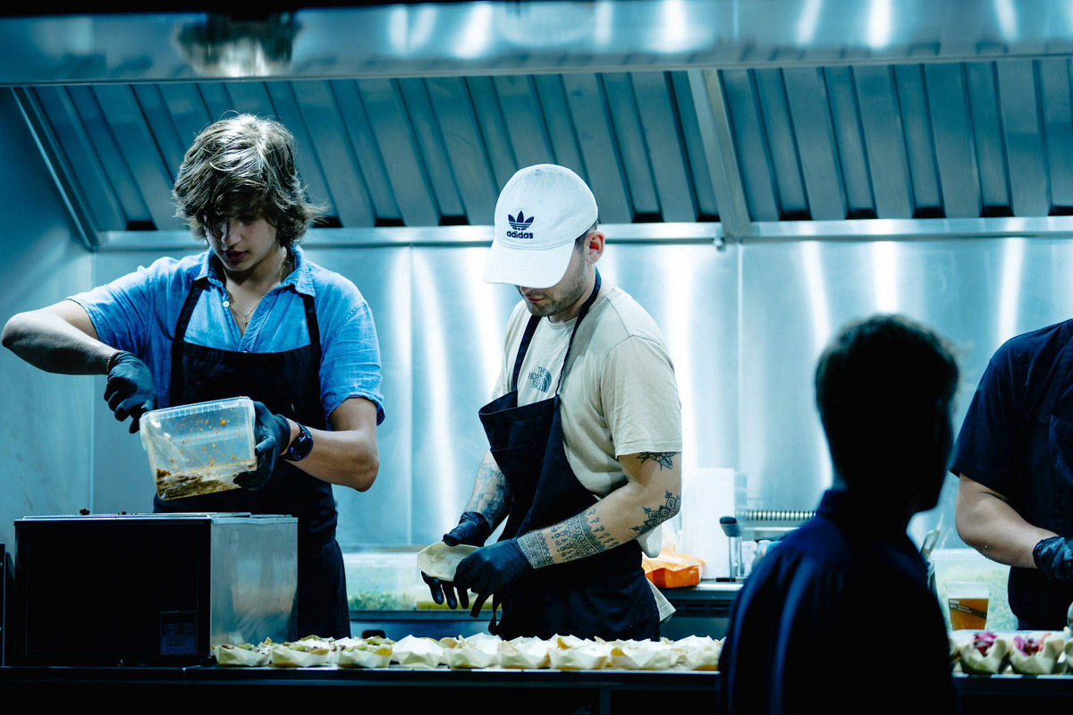 Food truck staff in black aprons preparing food at a steel counter under an extractor hood