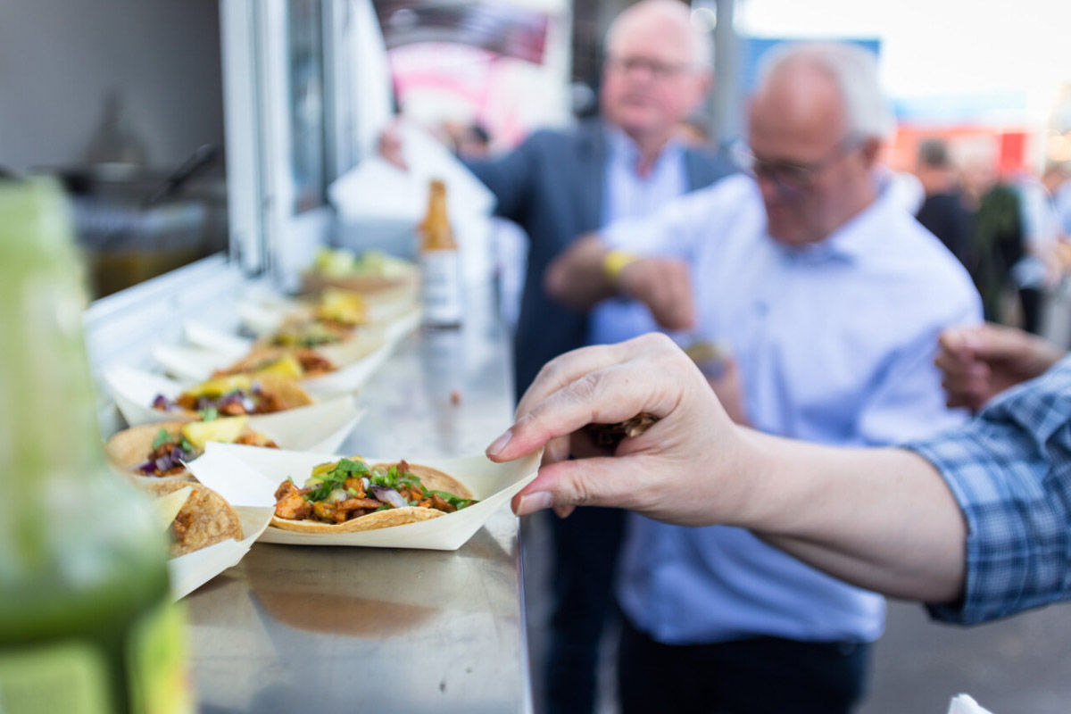 Guest picks up a chicken taco with fresh vegetables from a row on a food truck counter