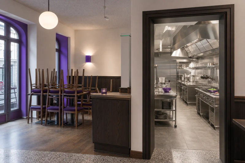 Leerer Gastraum mit gestapelten Stühlen und Blick in die Gastroküche