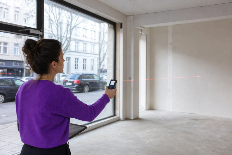 Leeres Ladenlokal mit großem Schaufenster, Architektin beim Aufmaß