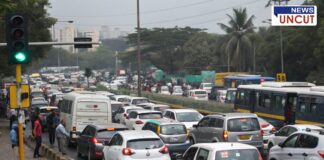 Heavy traffic congestion at Dapodi-Phugewadi due to a short-duration green signal. A long queue of vehicles, including cars, buses, and two-wheelers, is seen stuck at the traffic light. Pedestrians are walking along the roadside, highlighting the severe traffic bottleneck on this busy Pune-Pimpri-Chinchwad route.