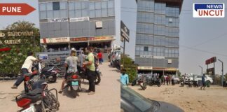 Outside view of Chakan Wines in Pune during Holi celebrations. People with colored faces are gathered near the entrance, some on motorcycles, while others stand in groups. The surroundings include a modern commercial building with a glass façade, parked vehicles, and a signboard of a nearby hotel. The scene captures the festive yet busy atmosphere of the area.