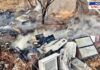 A scrapyard with burnt electronic waste and industrial debris, emitting smoke after a recent fire. Damaged refrigerators, metal scraps, and broken appliances are scattered across dry land. A charred tree stands in the background, and the ground is covered in ash. The "News Uncut" logo is visible in the top right corner.