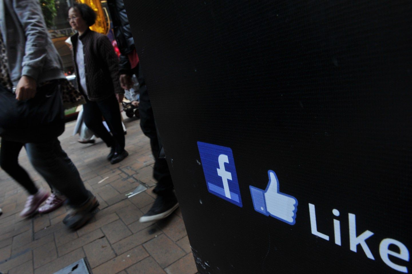 People walk by a Facebook logo and a thu