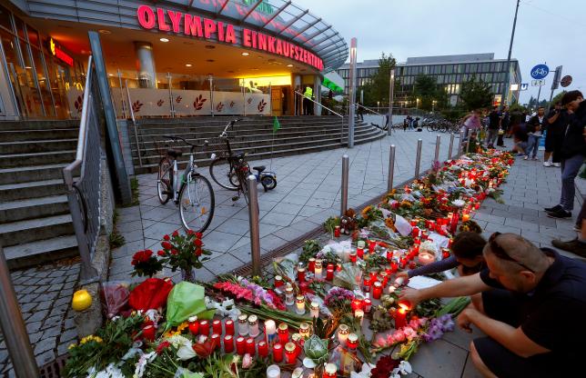People light candles beside flowers laid in front of the Olympia shopping mall, where yesterday's shooting rampage started, in Munich