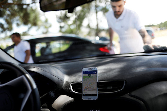 An Uber driver cleans his car as his cell phone shows the queue to pick up passengers departing Guarulhos International Airport in Sao Paulo