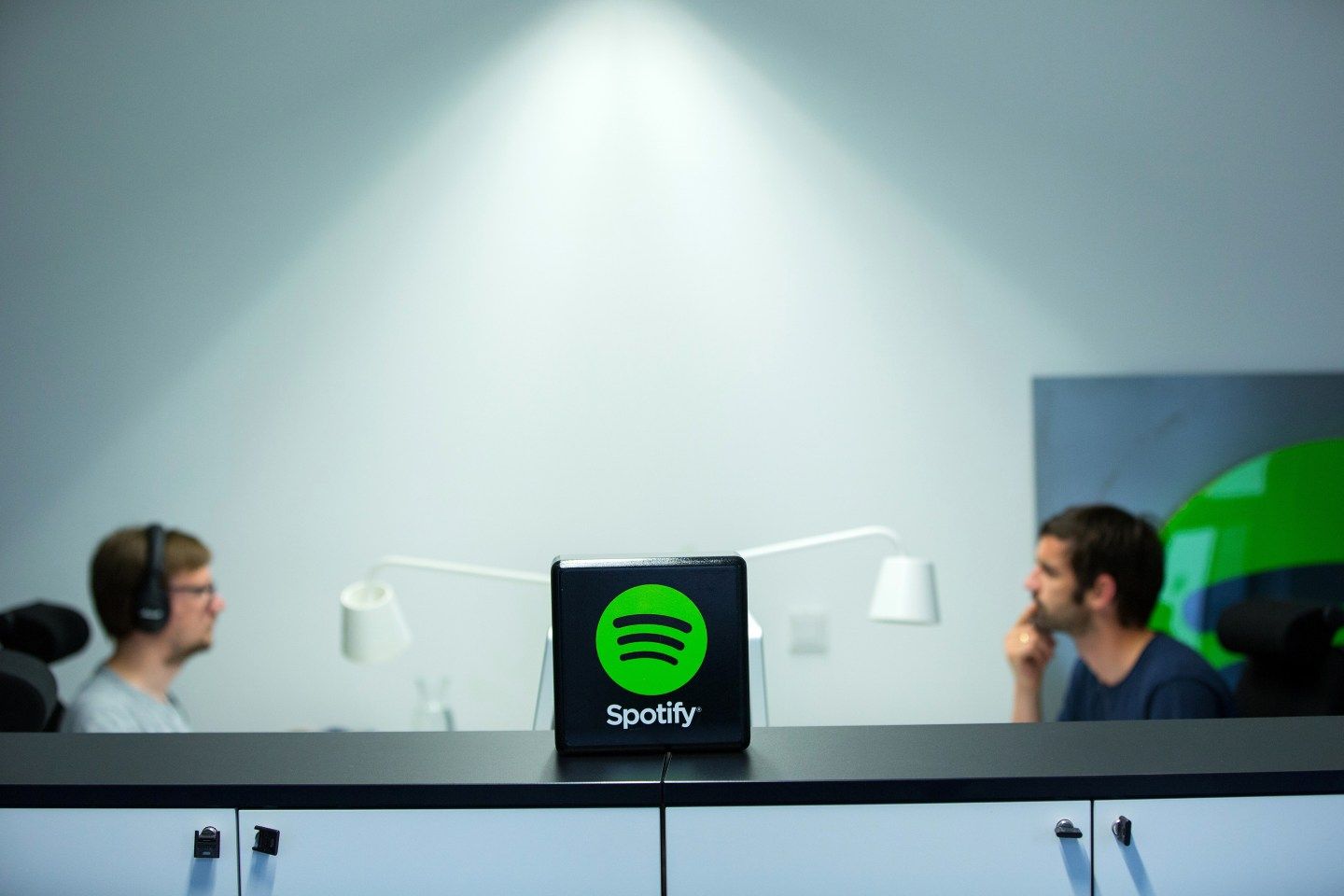 Spotify logo sits on a desk and employees sit on either side in the background