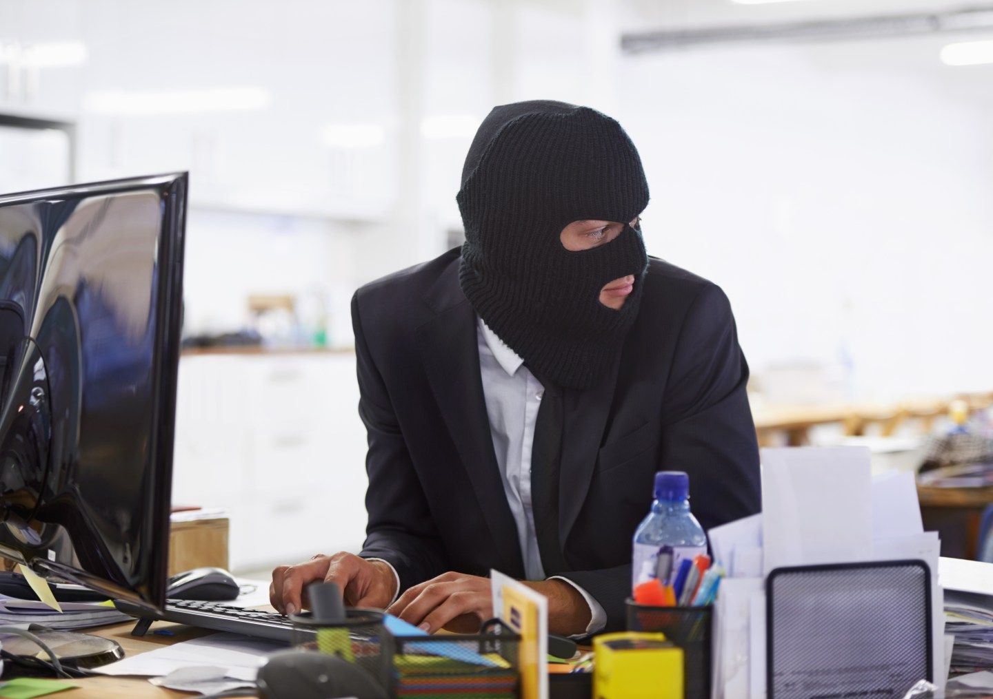 A hacker dressed in a black mask at a computer.