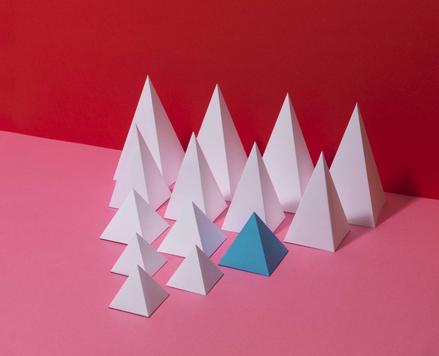 Group of white pyramids, one blue pyramid, on red background
