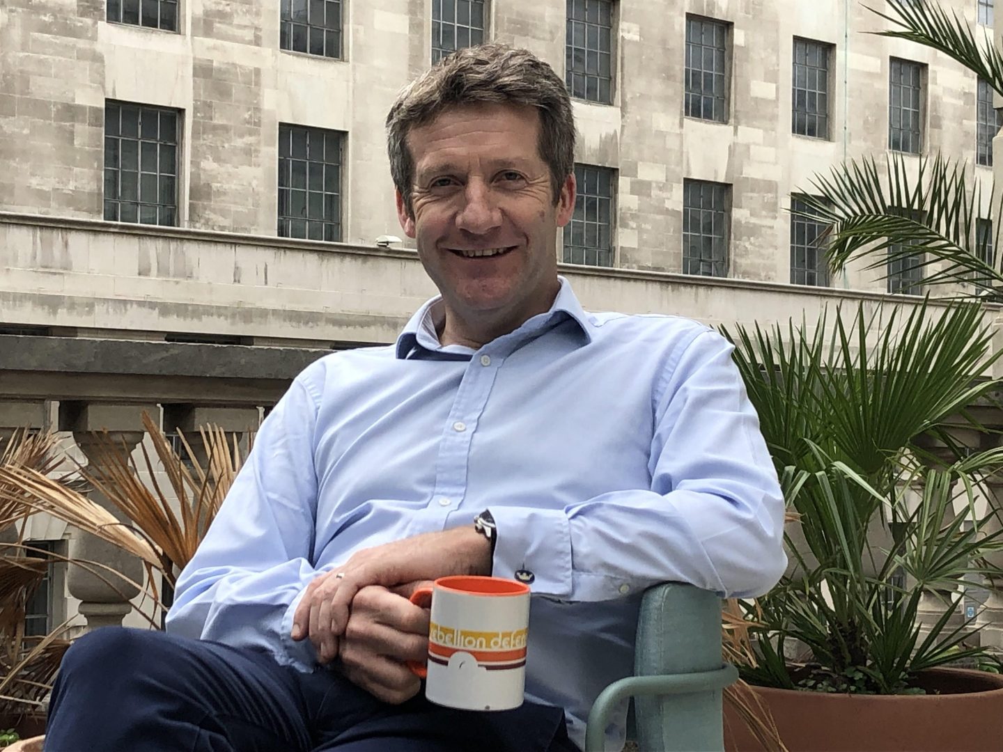 Photo of RAF Air Marshal Johnny Stringer in civilian clothes sitting with a Rebellion Defence coffee mug.
