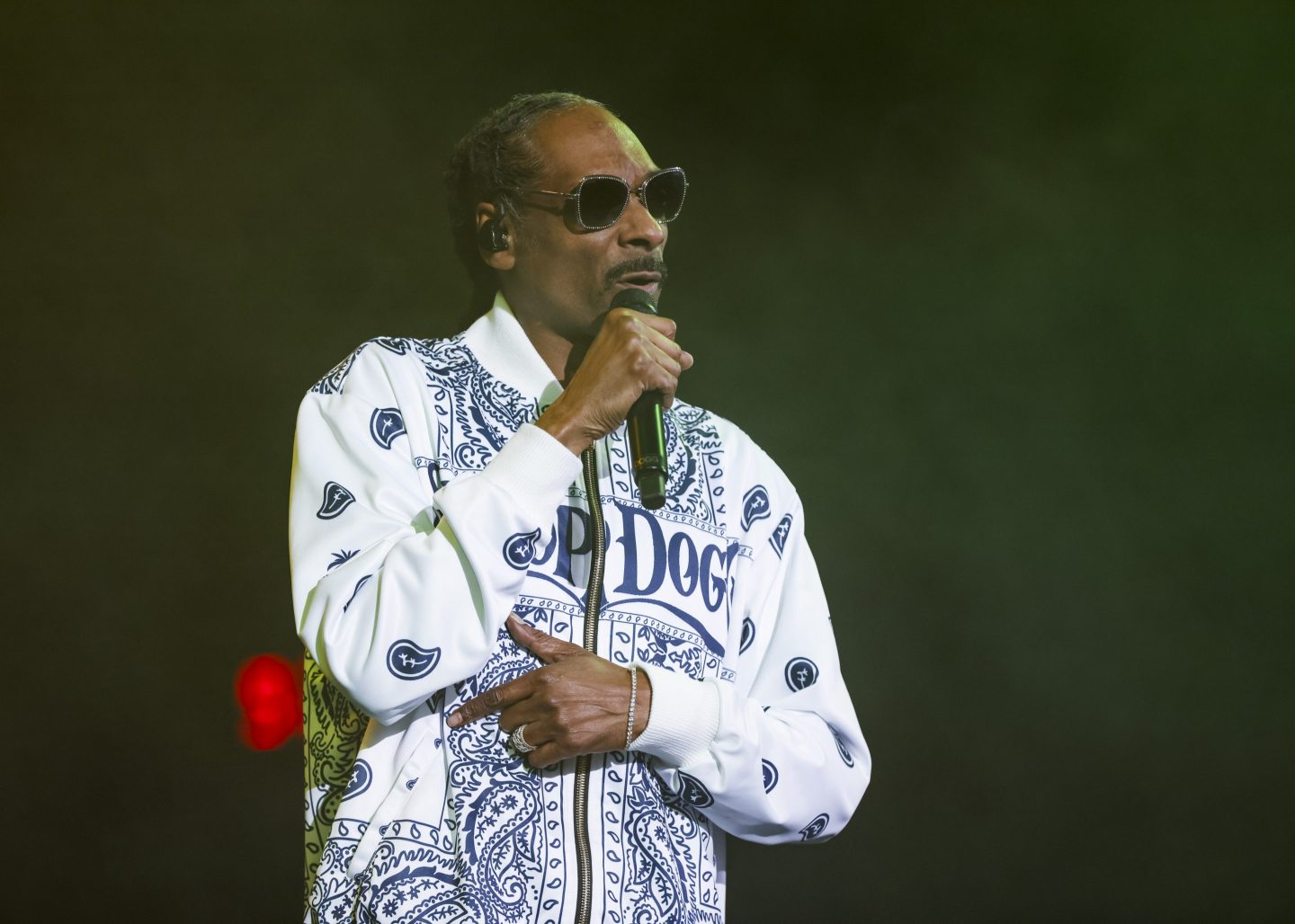 performer Snoop Dogg wearing a white jacket and sunglasses singing onstage