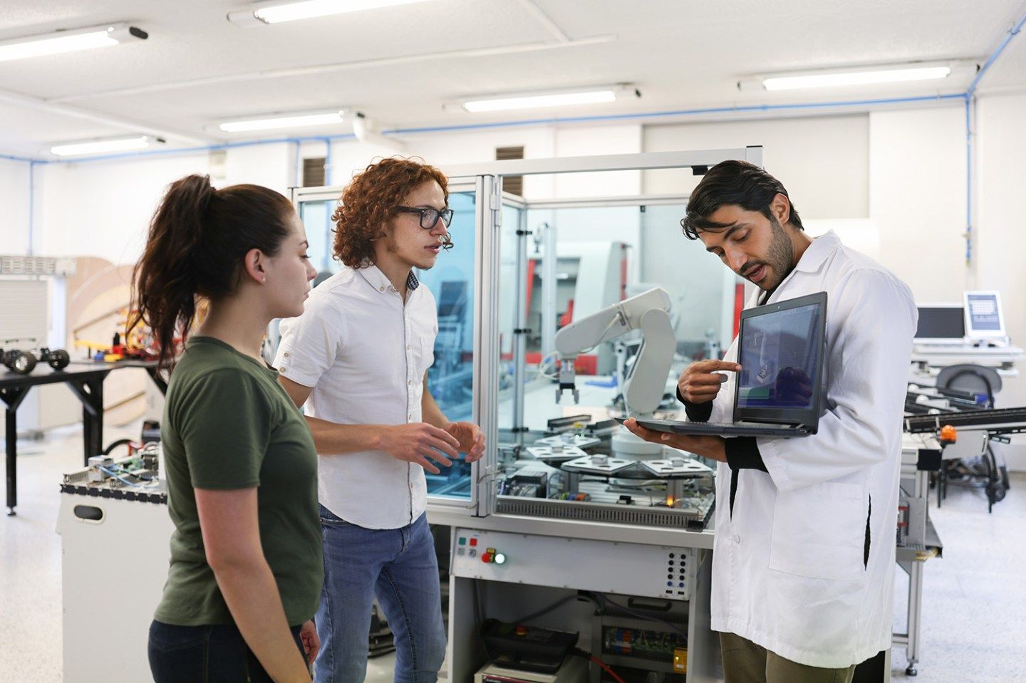 Teacher explaining something to a couple of college students in a robotics class - stock photo