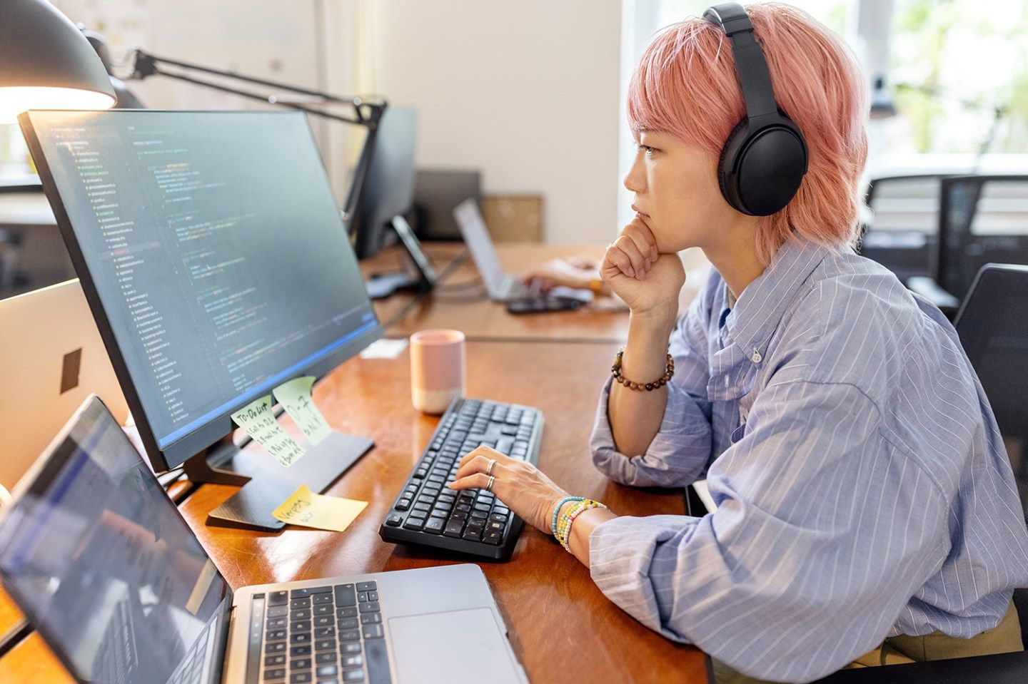 Side view of a woman computer programmer working at her desk at a startup company. Businesswoman wearing a headset looking at computer monitor and thinking while coding in office space.