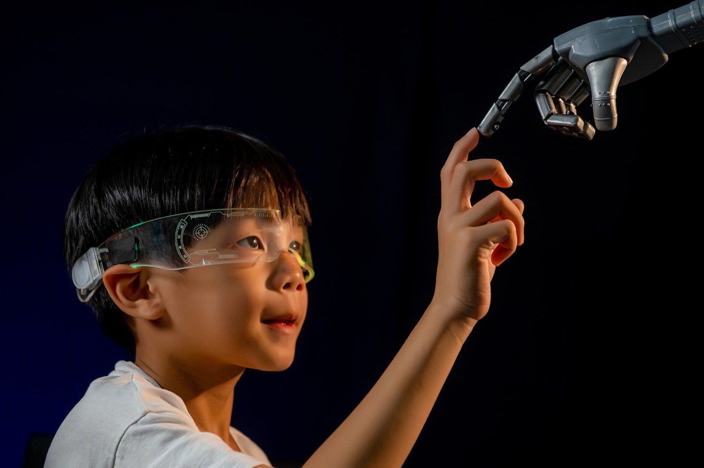 Robot hand touching human boy child hand on black background