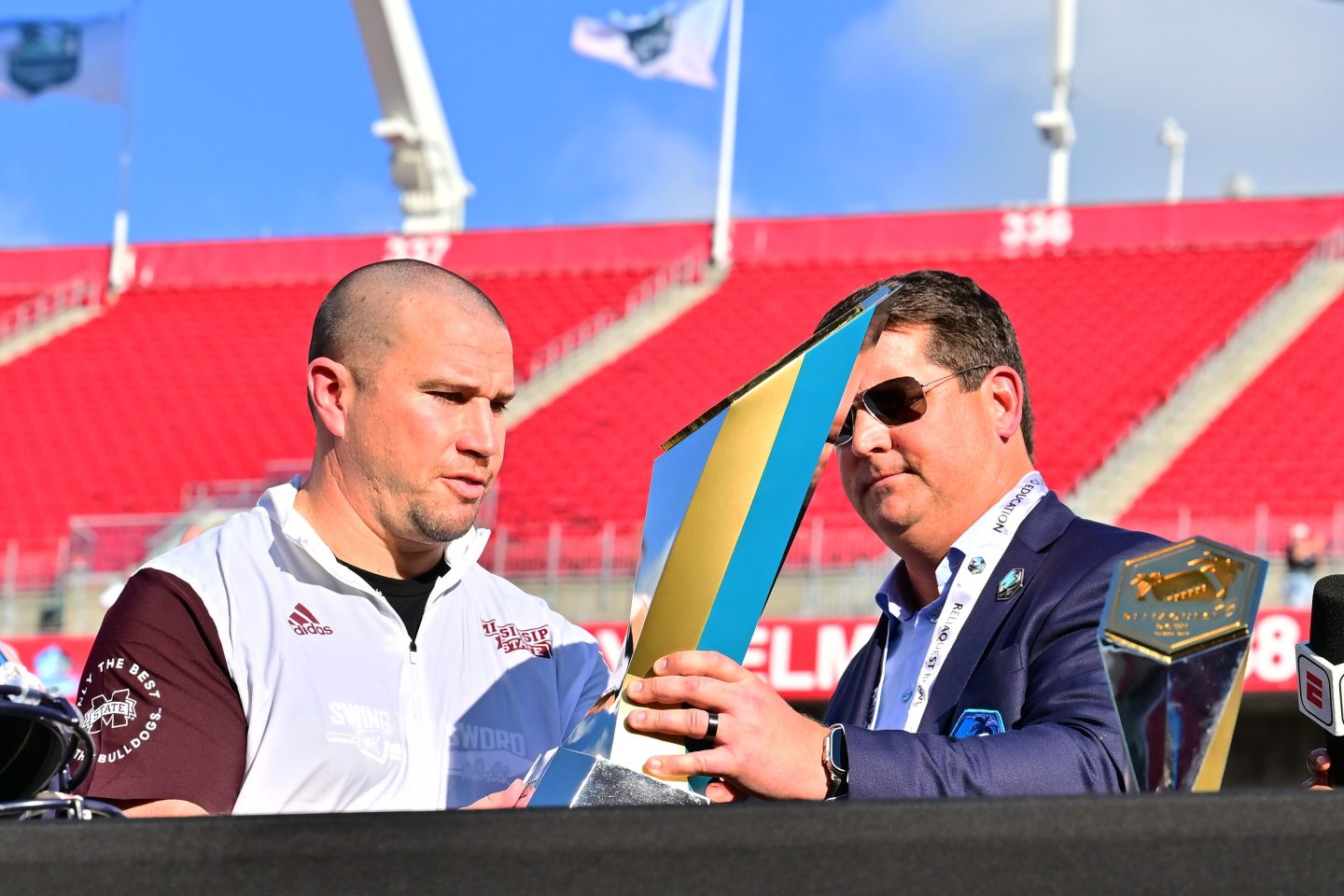 Brian Murphy (right), in sunglasses a sport coat, hands Zach Arnett a shiny trophy (left).