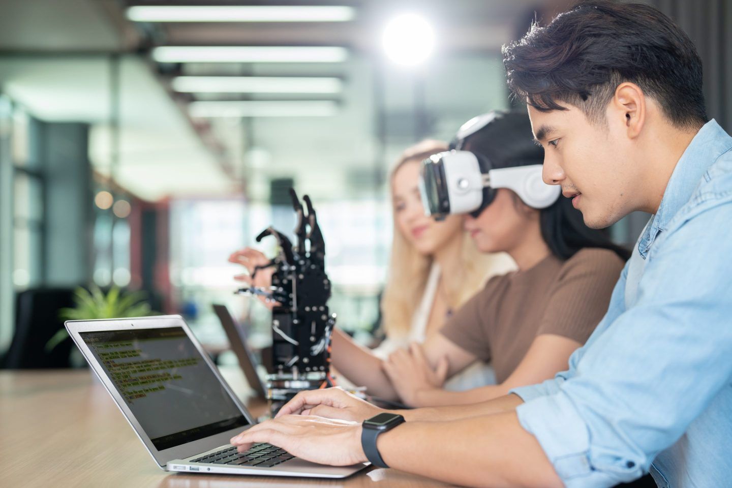 Man works on a laptop while a woman next to him wears a virtual reality headset.
