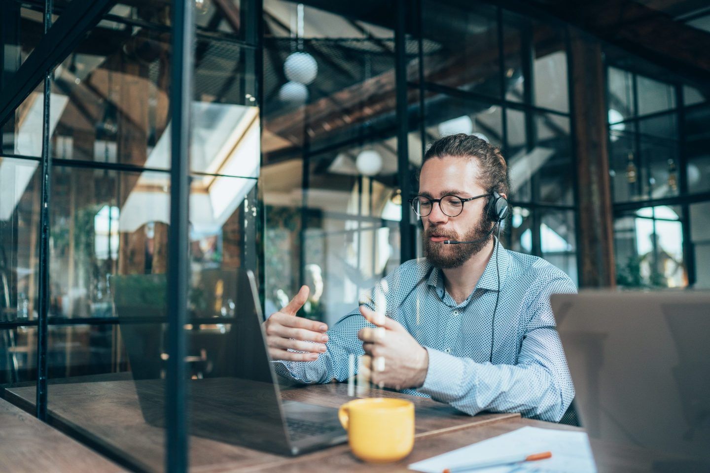 Young businessman with a headset on in a modern office talks to a laptop video call