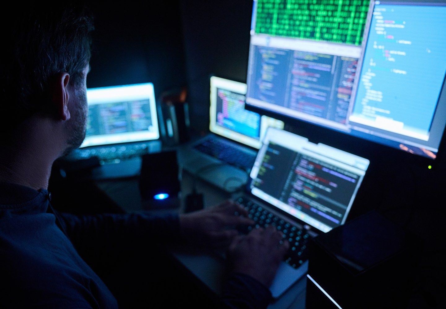 Man works on code in front of several computer screens