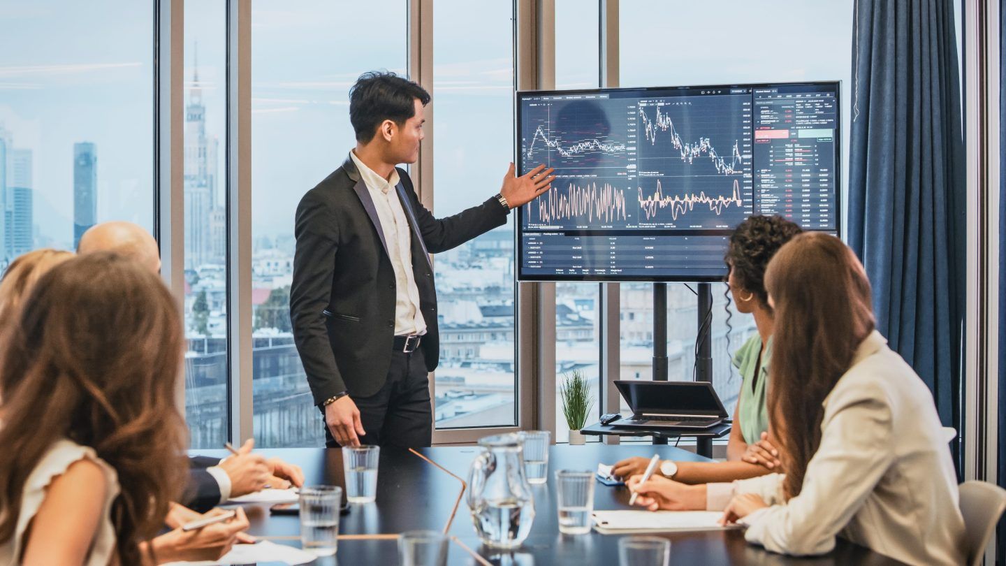 Man displays data on a screen to a conference room of individuals.