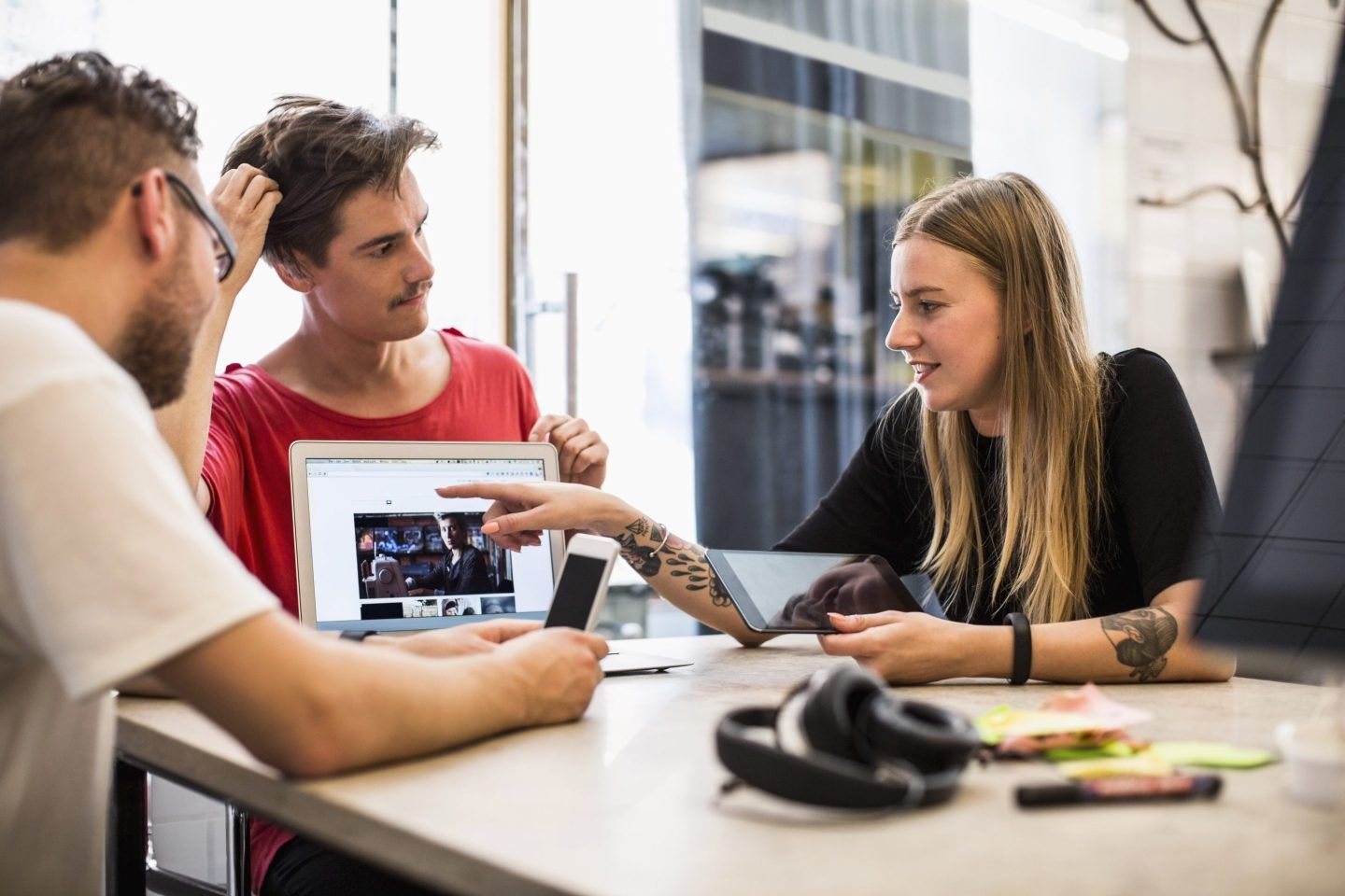 Business team sits at a table; woman points to an open laptop