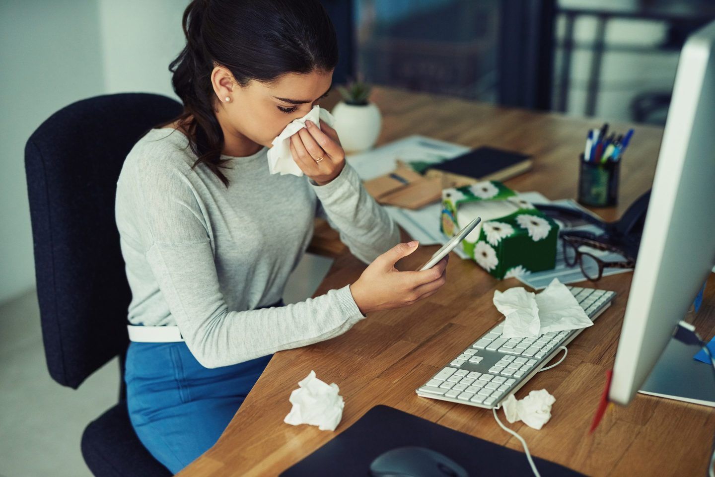 Shot of a young businesswoman at work blowing her nose