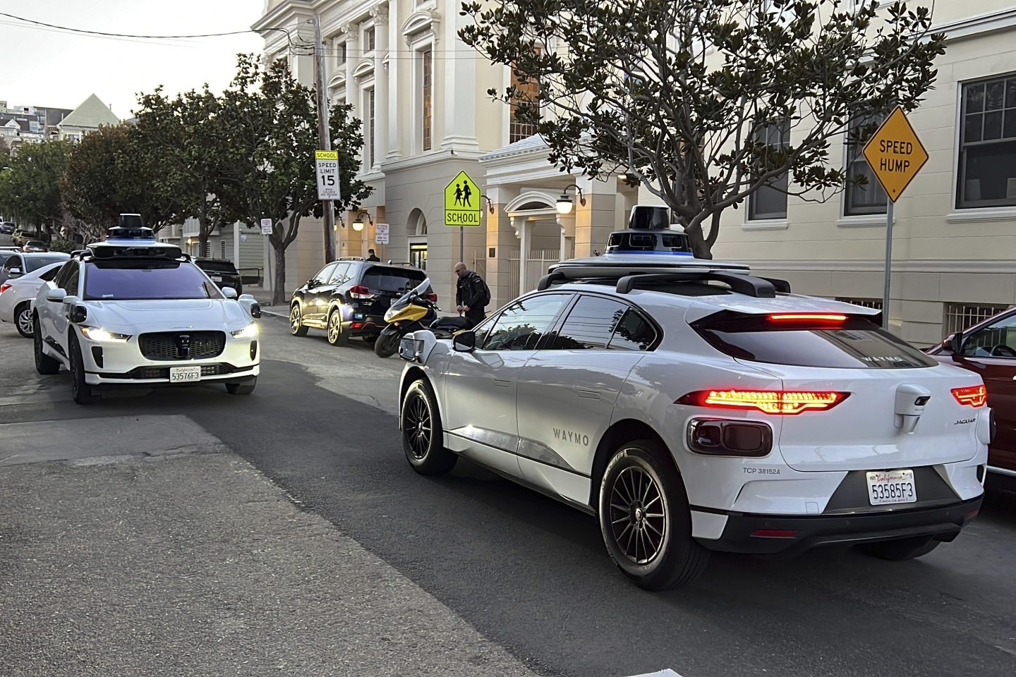 A pair of driverless Waymo cars sit parked on a beautiful street