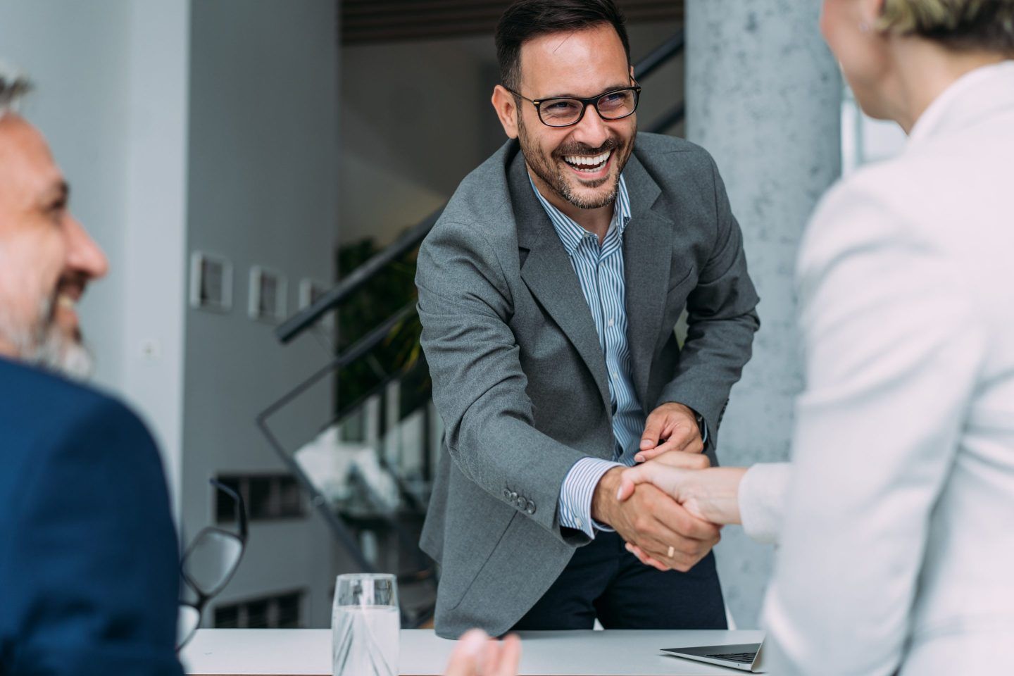 Business people handshaking across the table during a meeting in modern office. Group of business persons in business meeting. Three entrepreneurs on meeting in board room. Corporate business team on meeting in the office.