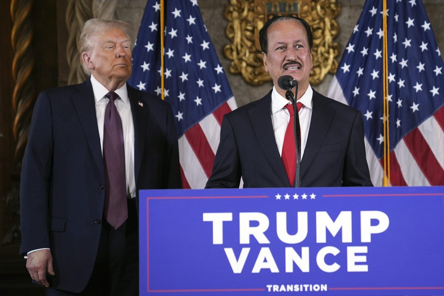 Donald Trump looks on as Dubai billionaire Hussain Sajwani stands at a podium and speaks into a microphone