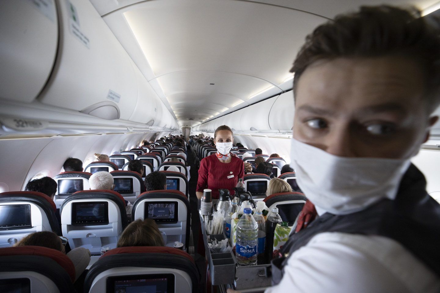 Two Turkish Airlines flight attendants in masks serving food and beverages in the plane cabin
