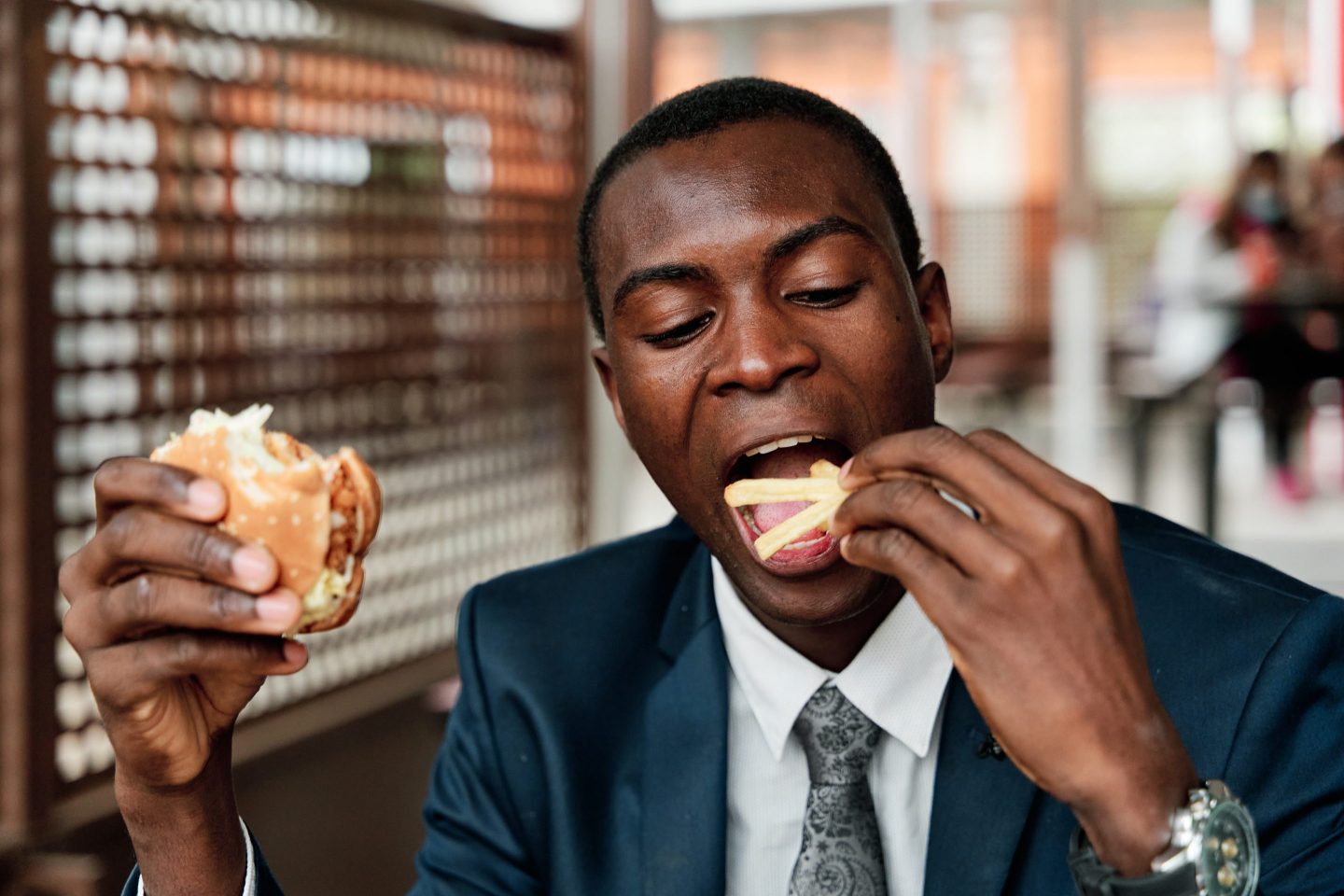 Young man holding a hamburger in one hand and fries in the other