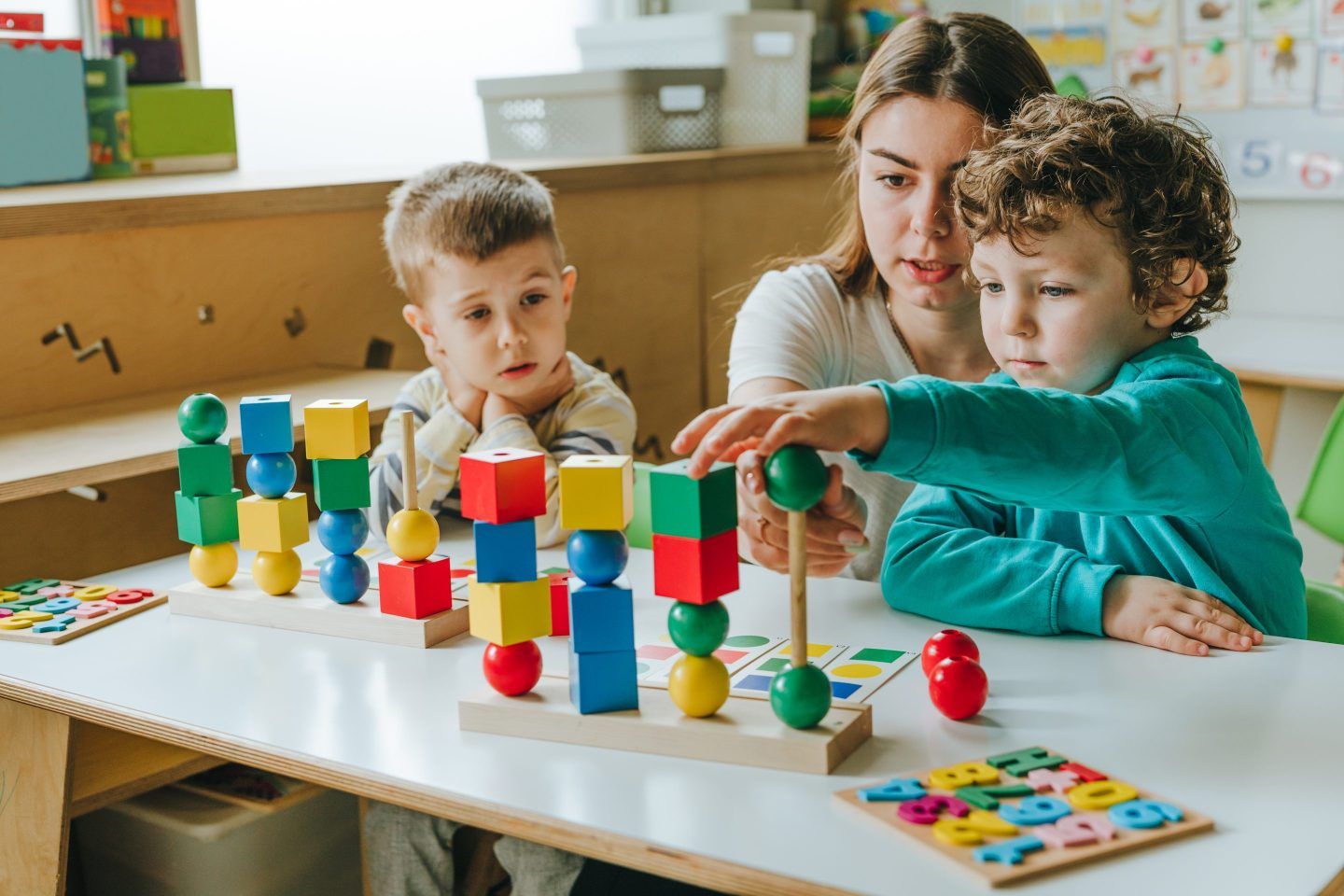 Female teacher helping little boy sort the cubes by color in a kindergarten.