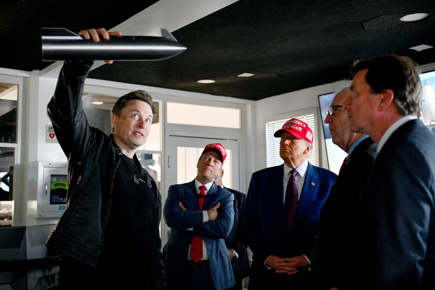 Elon Musk holds a metal rod in a demonstration in front of Donald Trump and a group of men.