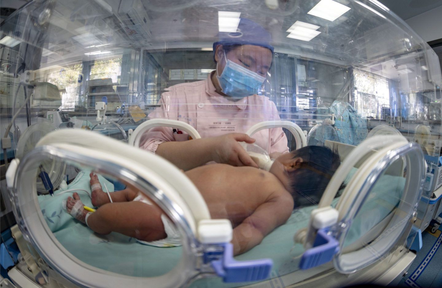 A masked nurse feeds a newborn infant in a neonatal unit in China.