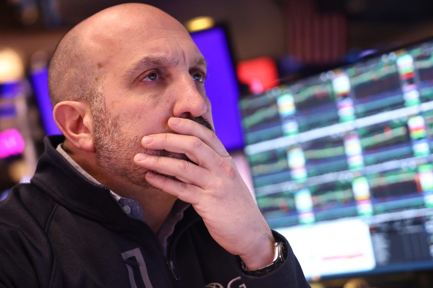 A man puts his hand over his mouth in concentration as he works the floor of The New York Stock Exchange.