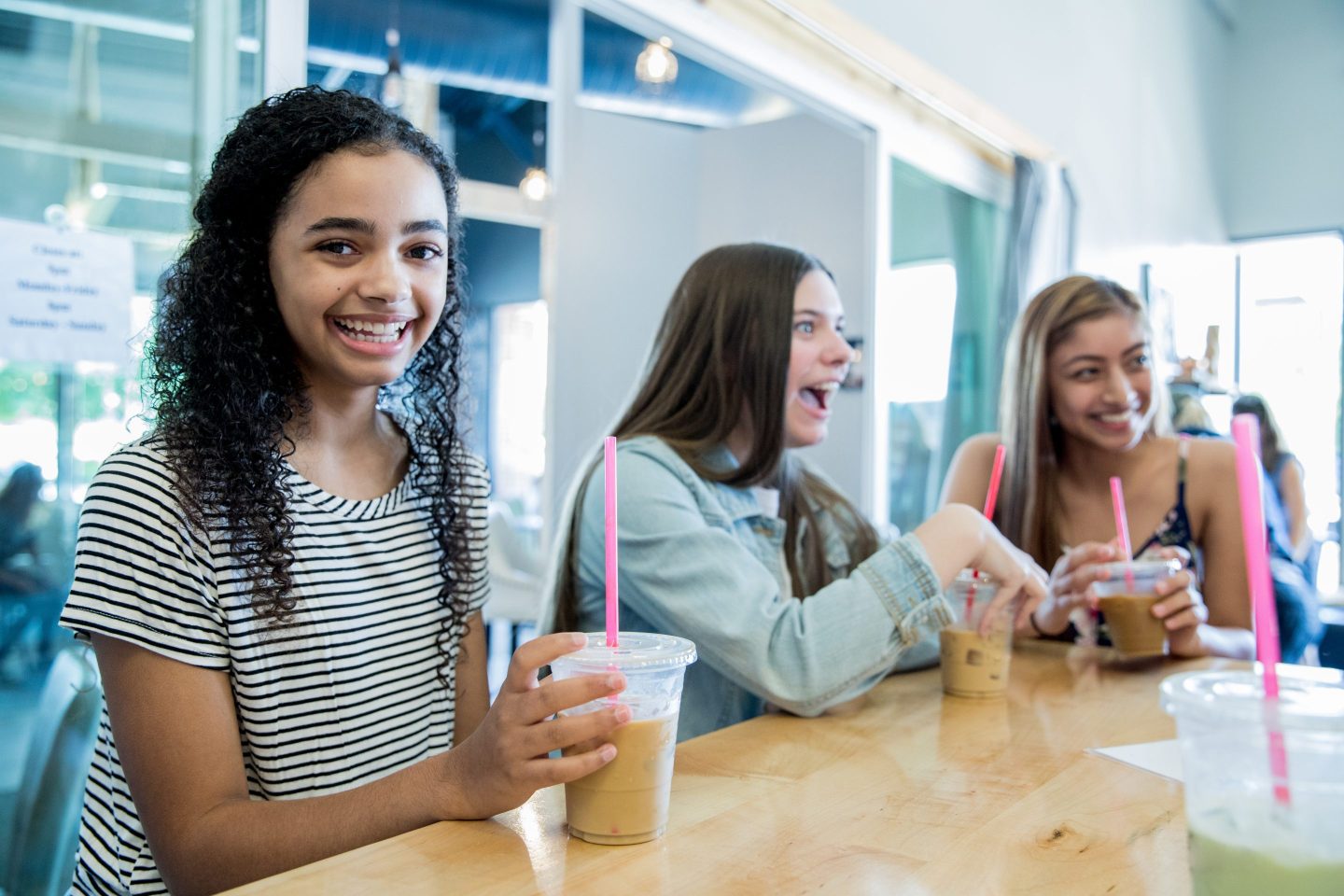 Three teen girls sitting around a table with iced coffee drinks