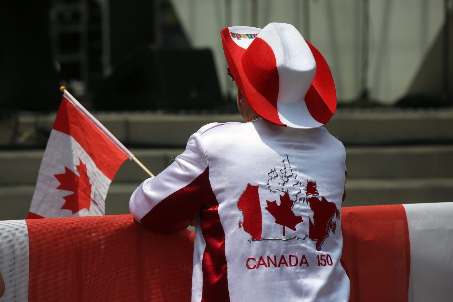 A person in a red and white cowboy hat, a Canada t-shirt holding a Canadian flag.