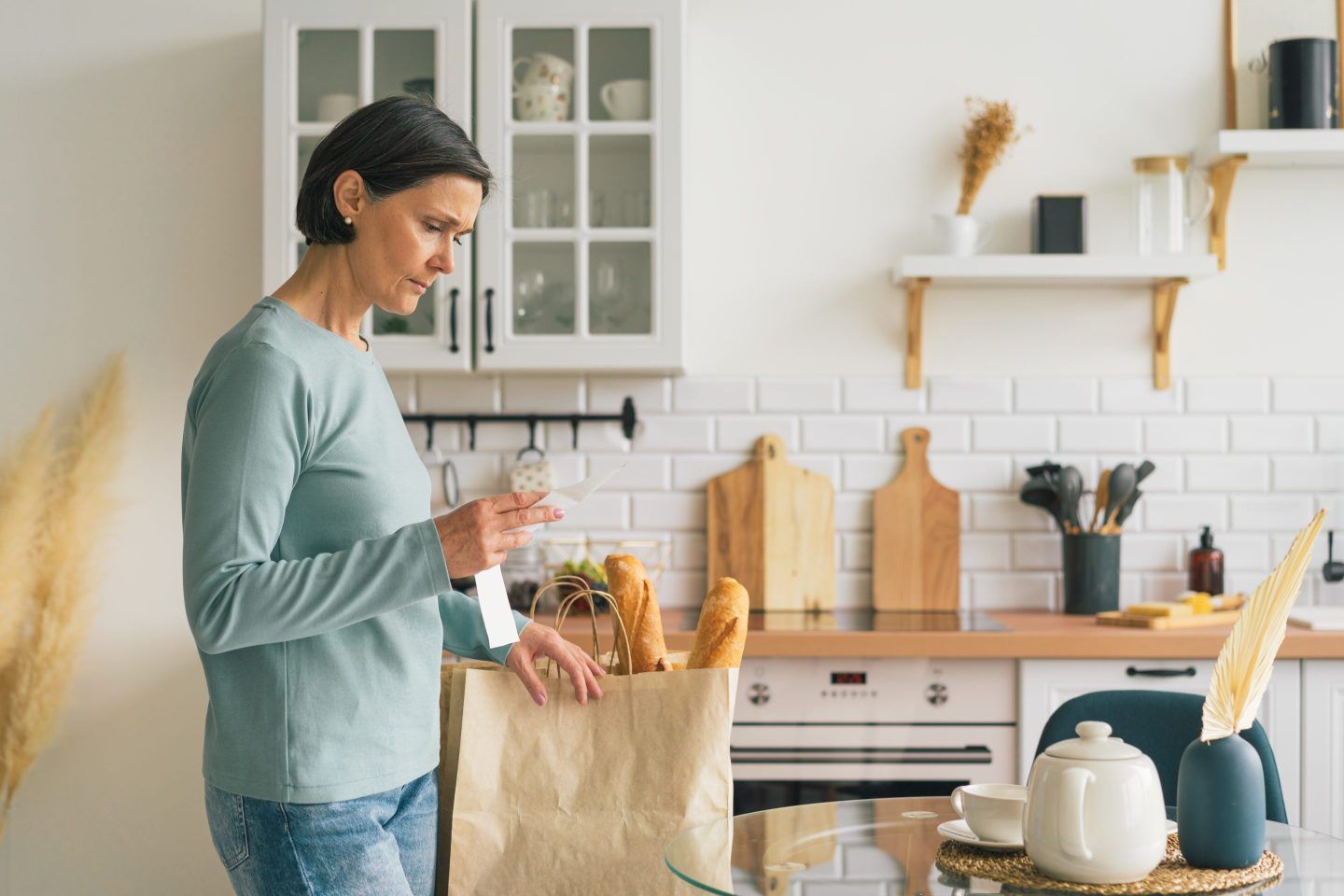 A person standing in a kitchen looking at a receipt.