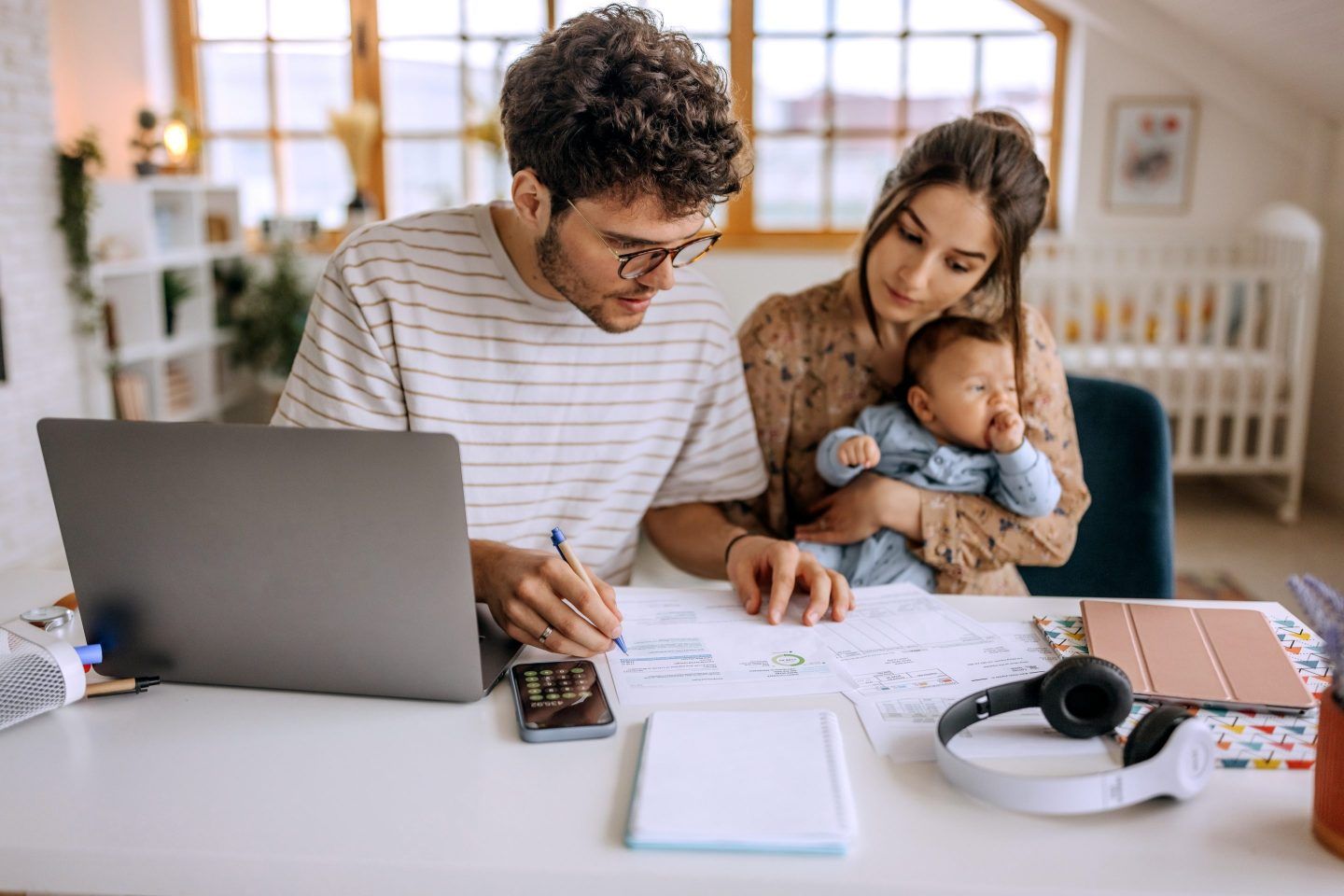 A young couple with a baby takes a look at paperwork in front of a laptop and calculator