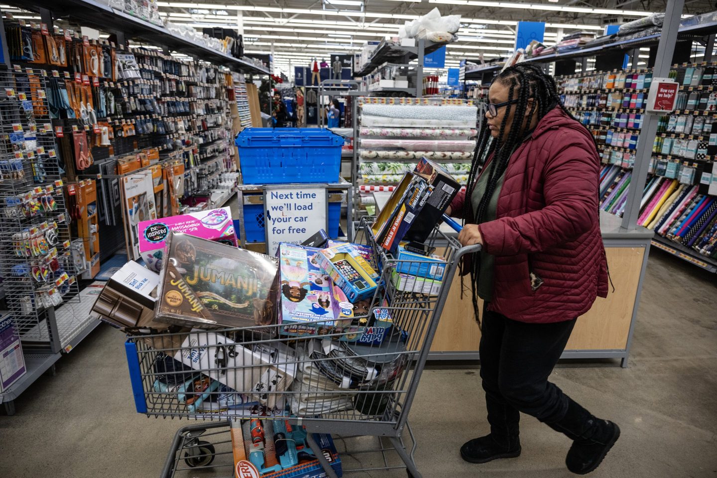 A shopper in a Walmart pushing a large cart stuffed with merchandise