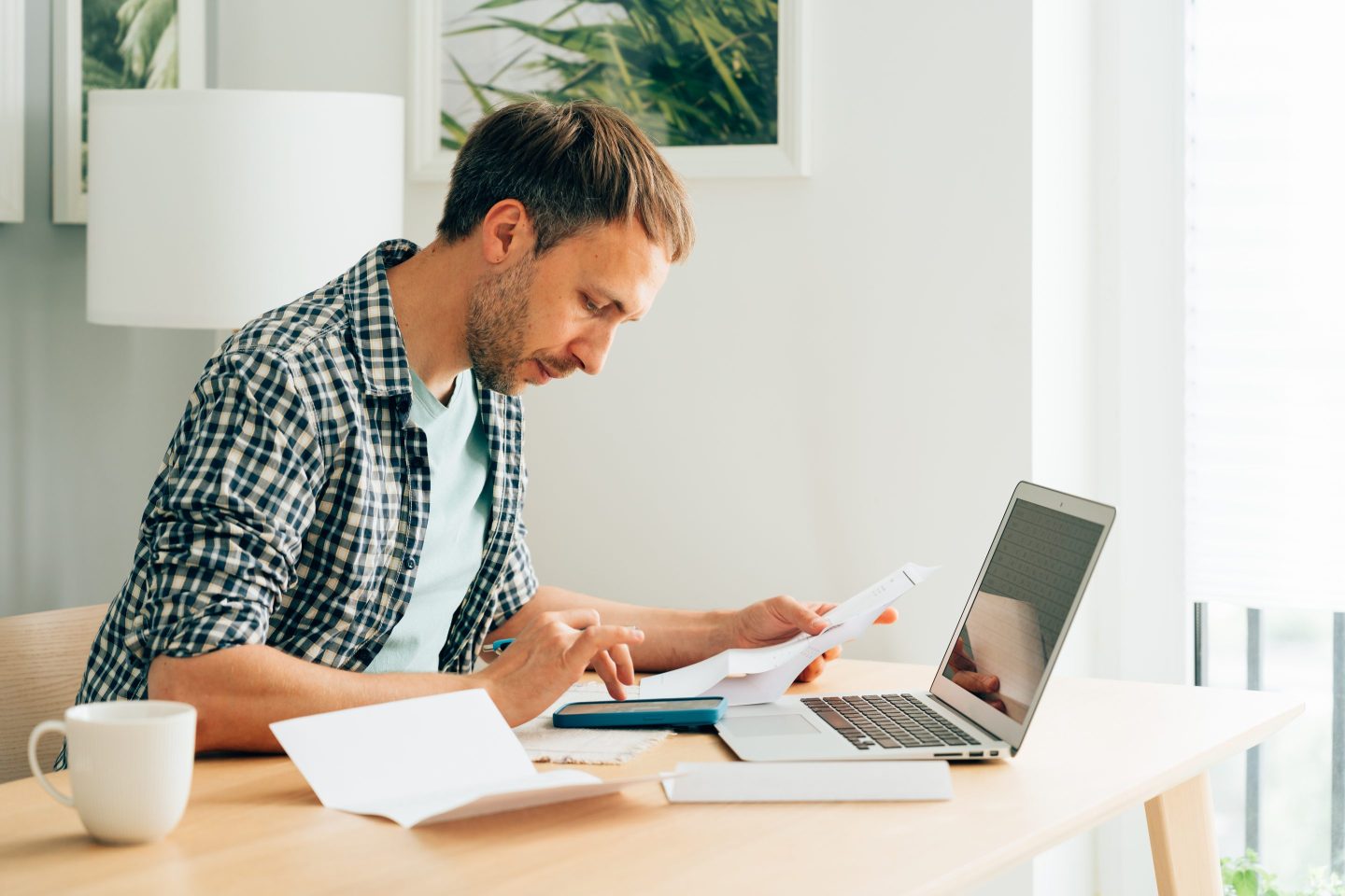 A person sitting a desk, holding papers and tapping on a phone.