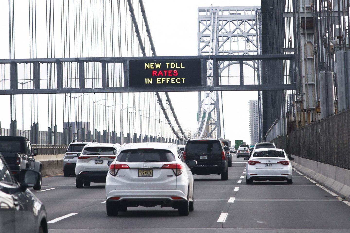 Cars pass over a bridge with a sign warning drivers about new toll rates in effect
