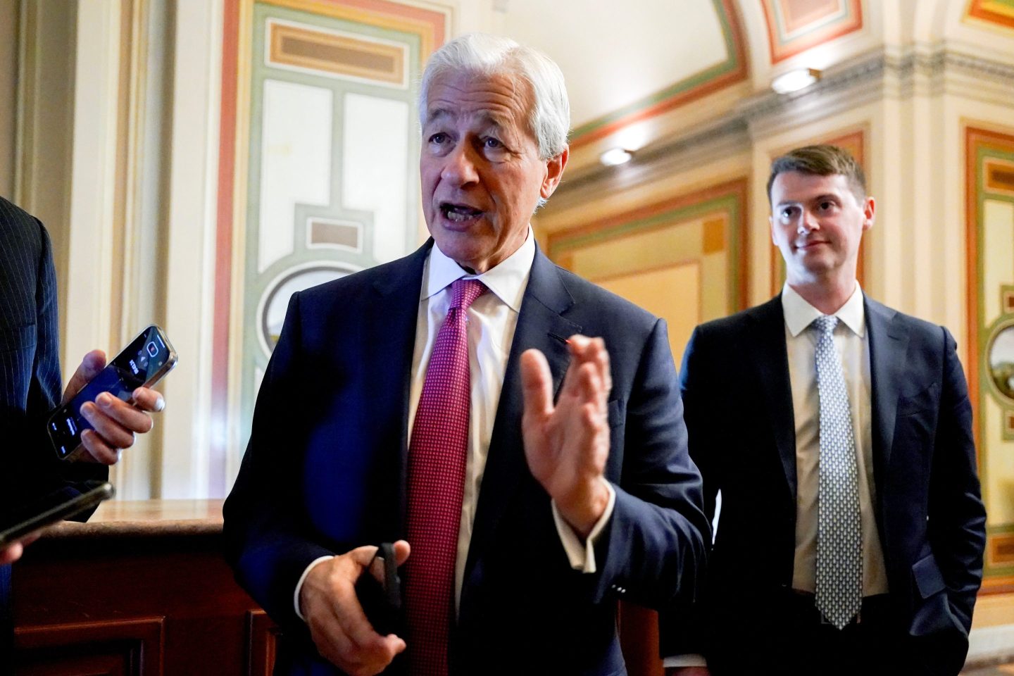 Jamie Dimon lifts his left hand up as he talks to reporters in the U.S. Capitol.