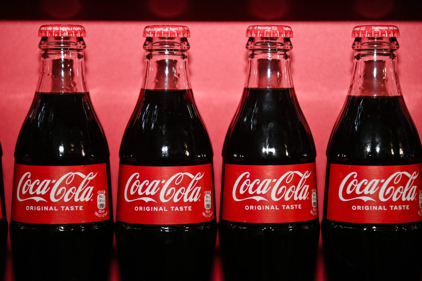 Glass Coca-Cola bottles lined up on red background