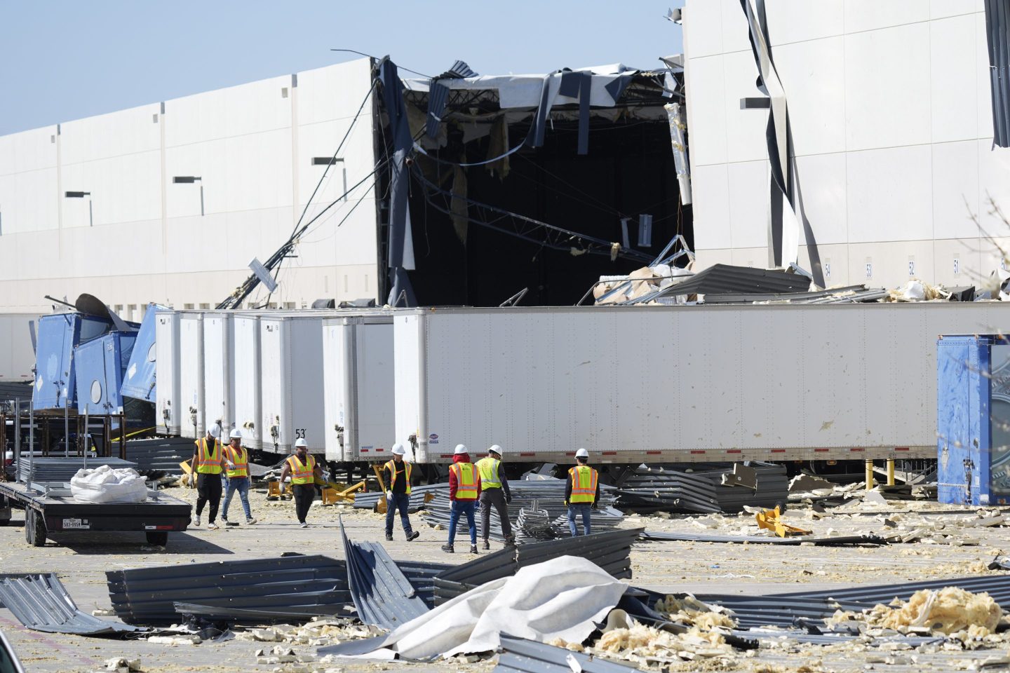 Workers walk outside a damaged warehouse after storms moved through on March 4, 2025, in Lewisville, Texas.