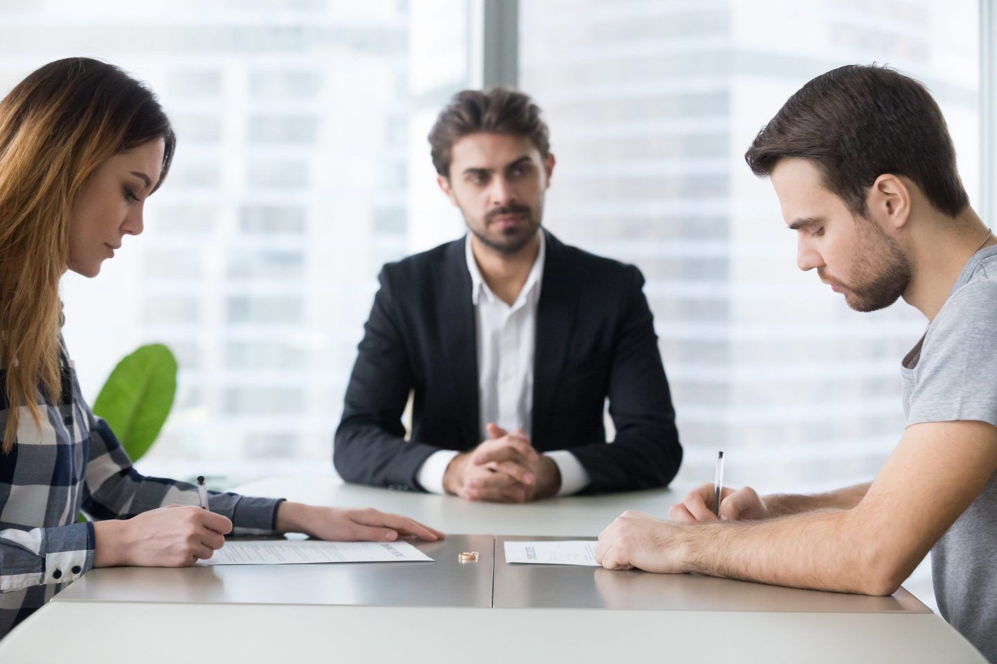 A man and woman sitting on opposite sides of a table in front of a man who is a divorce lawyer