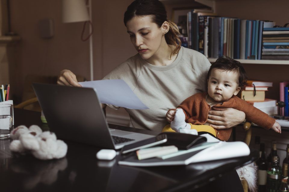 Female professional reading document while sitting with male toddler at home