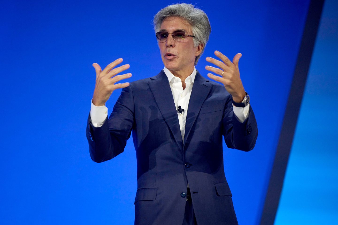 Bill McDermott, chief executive officer of ServiceNow Inc. on stage, in front of a blue background, gesturing with both hands.