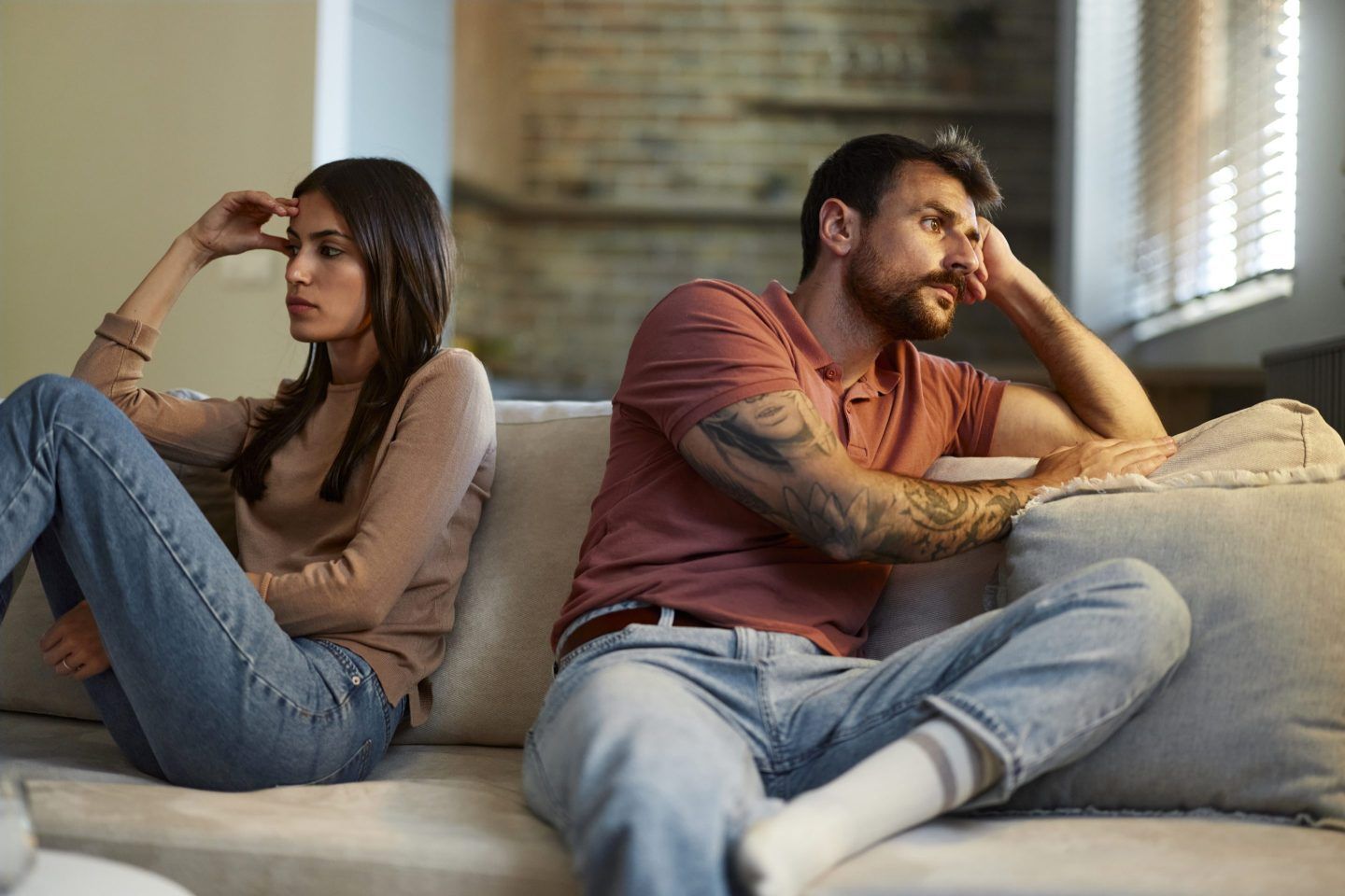 Worried couple sitting back to back on sofa at home