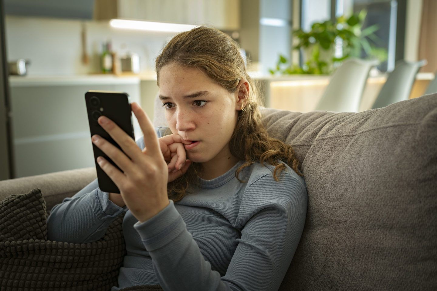 Nervous woman looks at her phone while biting her nail.